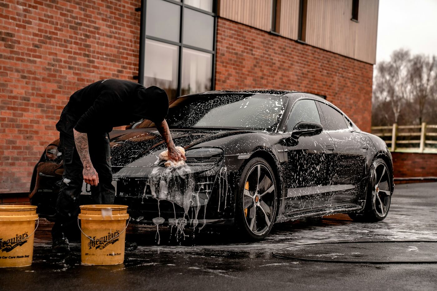 A detailer hand washing a black car with a sponge and thick suds